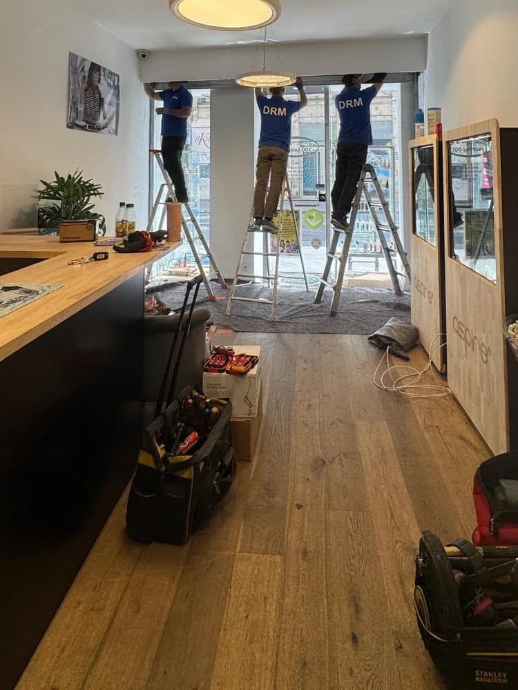 Équipe de trois techniciens DRM posant un rideau métallique derrière la vitrine d’une boutique