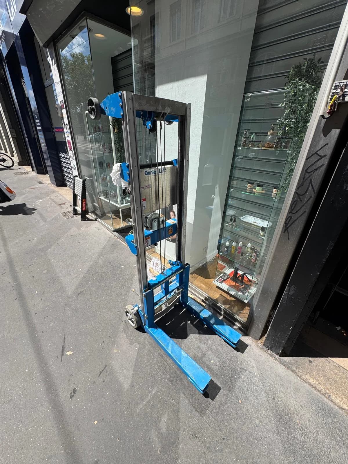 Lève-rideau installé sur le trottoir devant une boutique, pendant la pose d’un rideau métallique