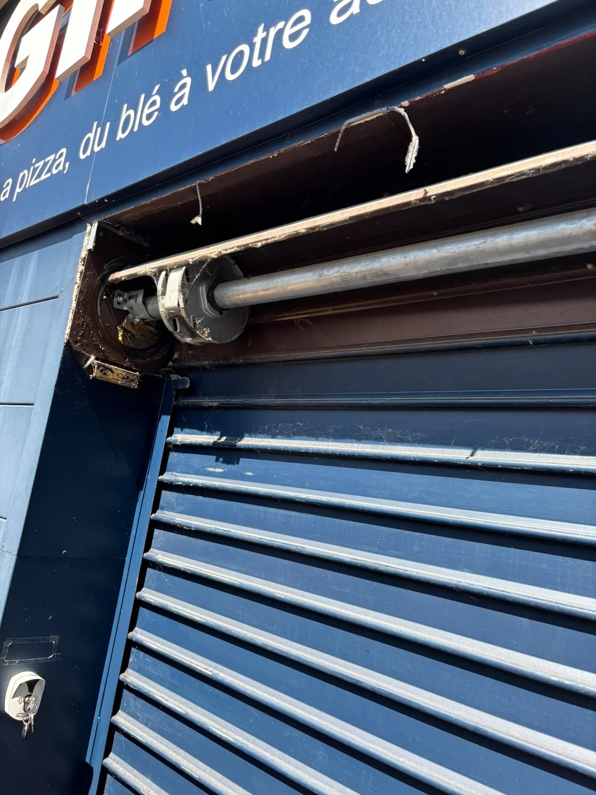 Axe et moteur central d'un rideau métallique sous le bandeau d'une enseigne