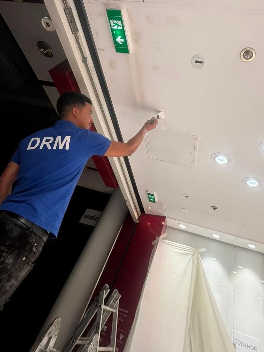 Technicien DRM en finition au plafond, au-dessus d’un rideau métallique
