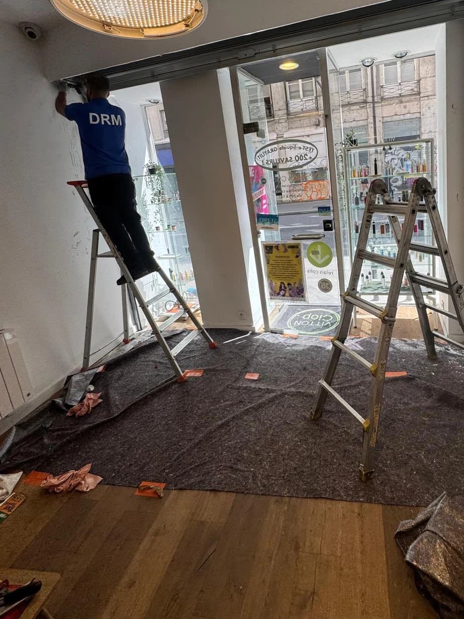 Technicien DRM posant un rideau métallique derrière la vitrine d’une boutique