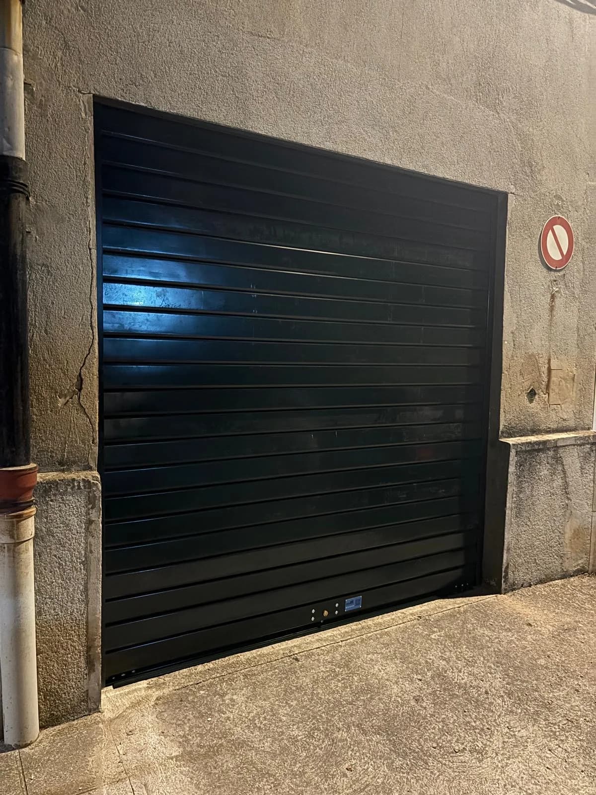 Rideau métallique neuf laqué foncé fermé sur une entrée de garage donnant sur rue