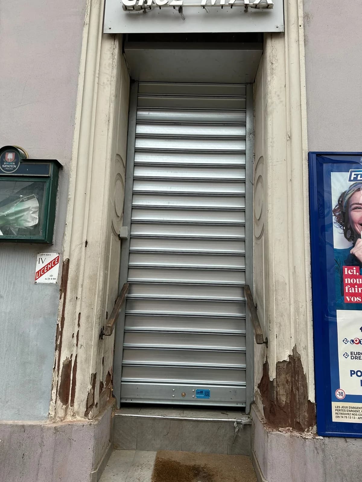 Petit rideau métallique neuf fermé devant la porte d’entrée d’un bar-tabac