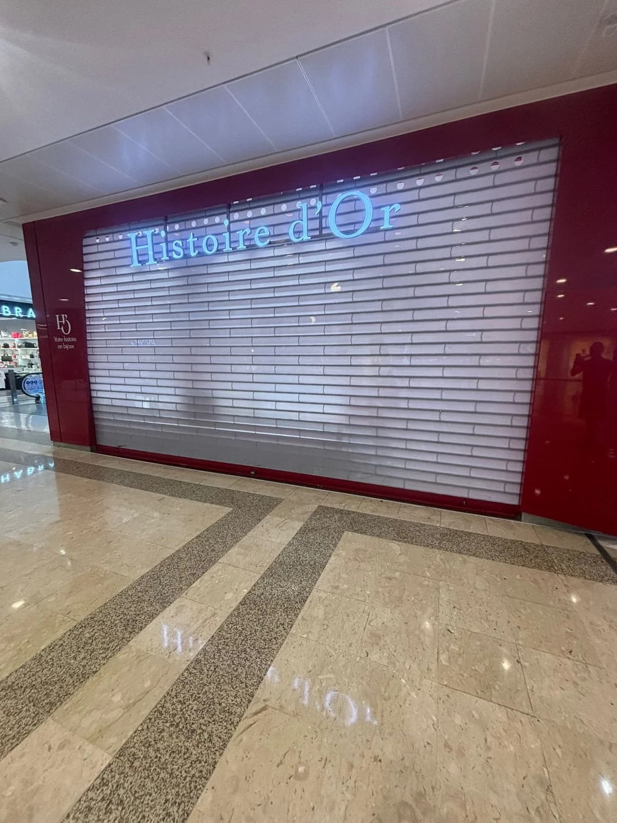 Rideau polycarbonate fermé devant une bijouterie en galerie commerciale, enseigne éclairée visible au travers